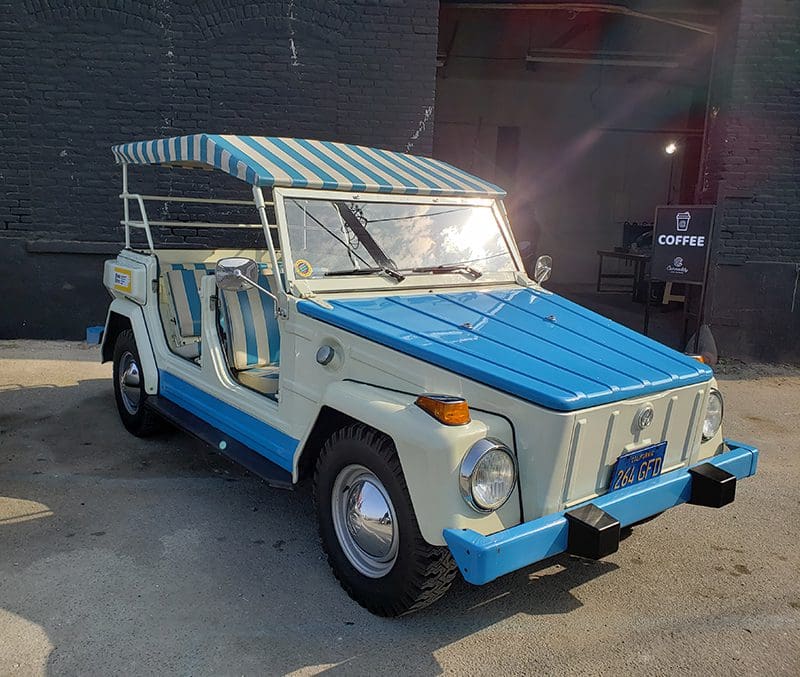 Vintage blue and white convertible car with striped canopy parked indoors.