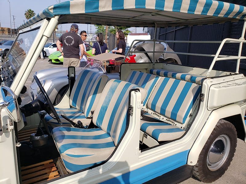 Vintage car interior with blue and white striped seats at a gathering.