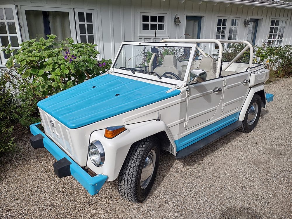 Vintage white and blue convertible car parked outside a house.
