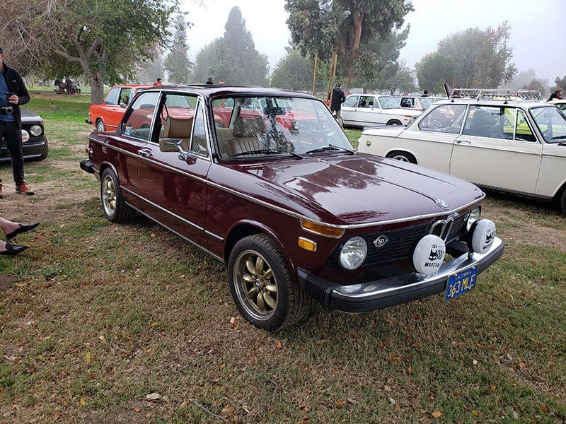 Classic maroon vintage car parked on grass, decorated with flowers.