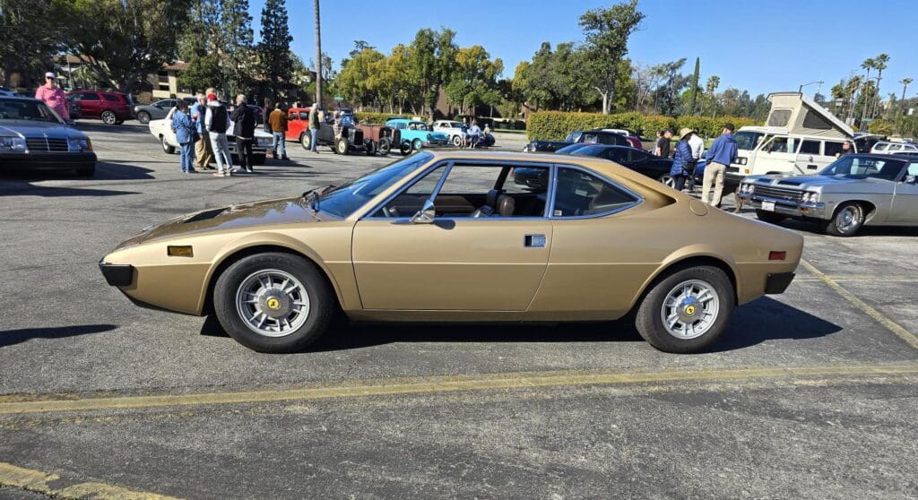 Classic gold Lotus Europa sports car parked outdoors on a sunny day.