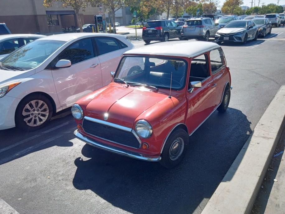 A classic red Mini Cooper parked in a sunny parking lot.