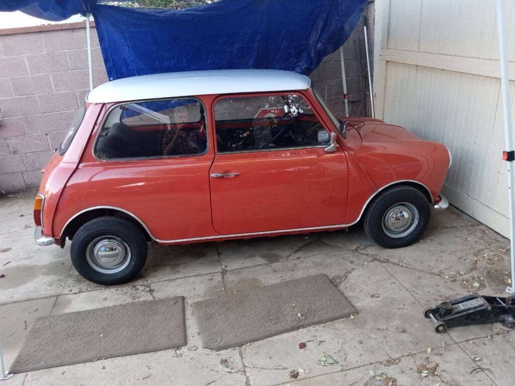 Classic red Mini Cooper parked under a blue tarp.