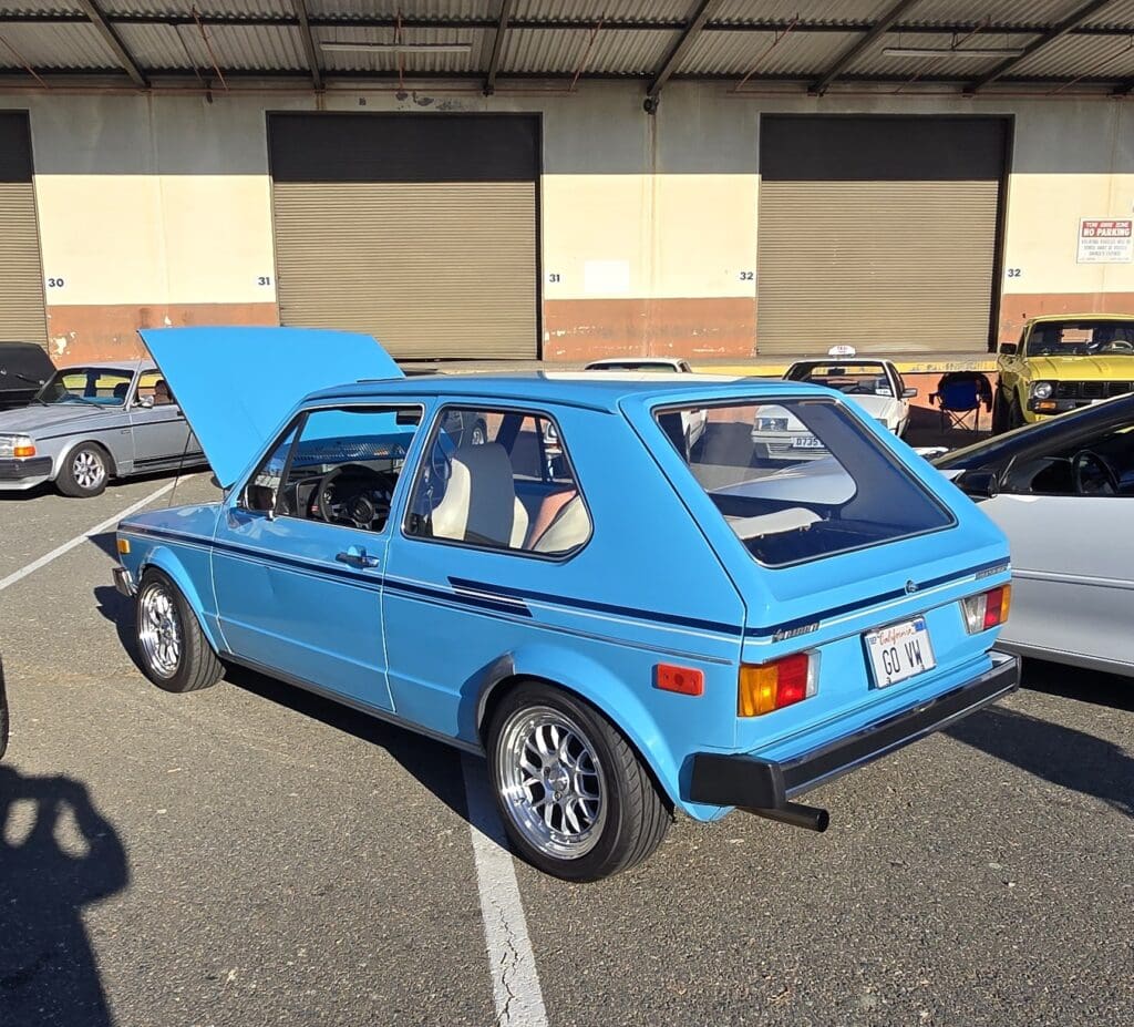 Classic blue hatchback car with its hood open in a parking lot.