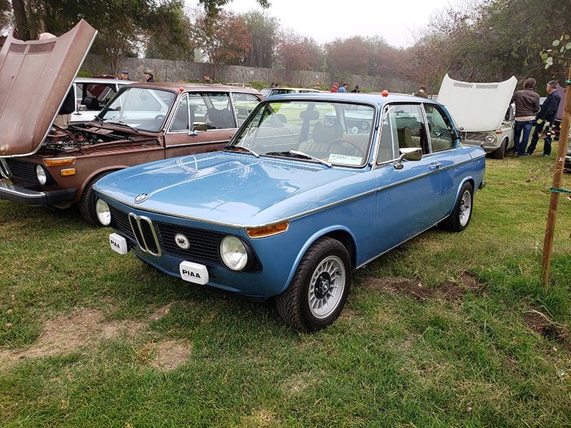 Classic blue BMW 2002 car parked on grass among other vintage cars.