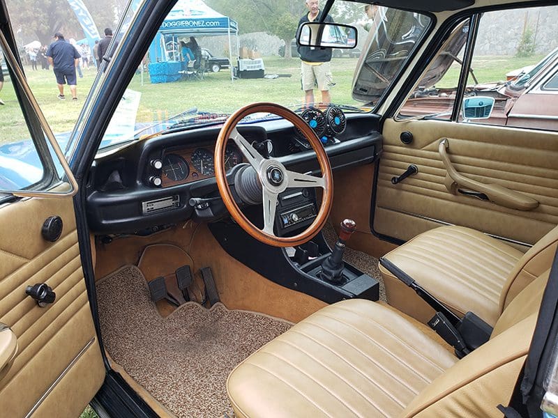 Vintage car interior with wooden steering wheel and tan seats.