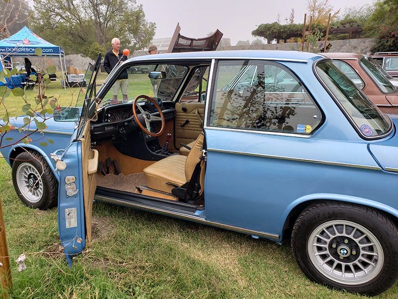 Rusty blue car with open doors parked on grass.