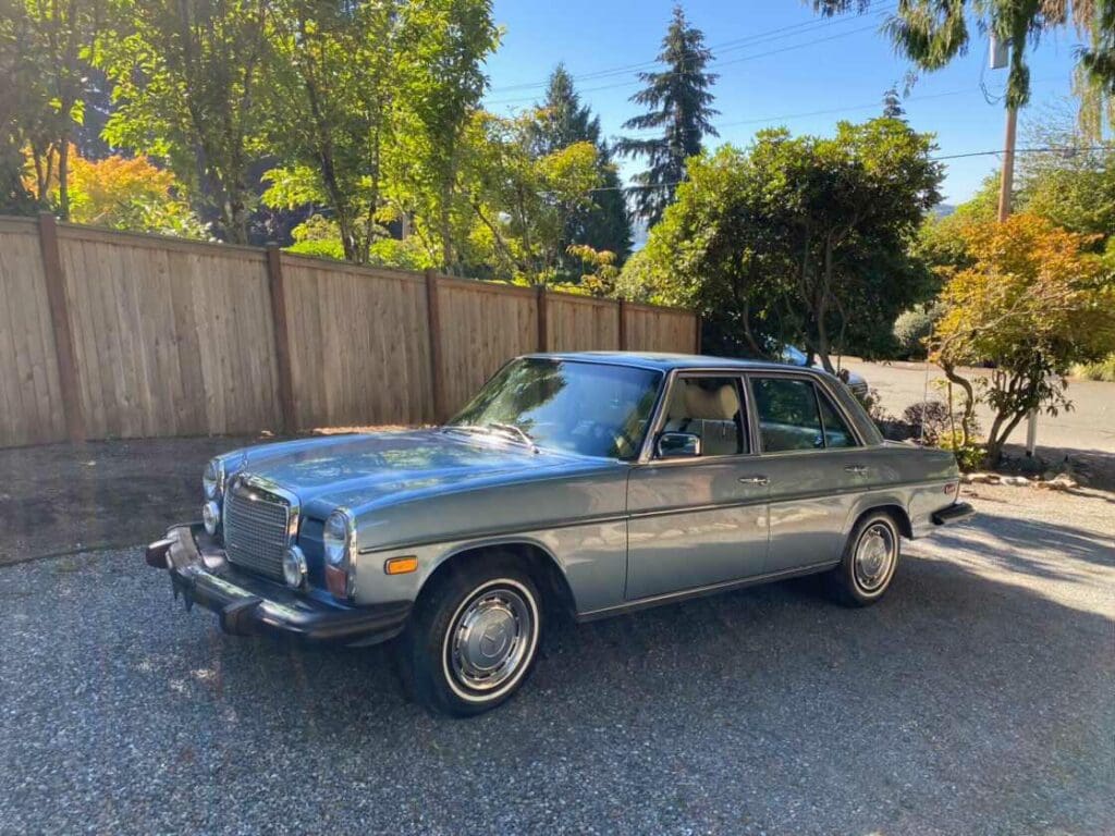 Classic vintage car parked beside a wooden fence on a sunny day.