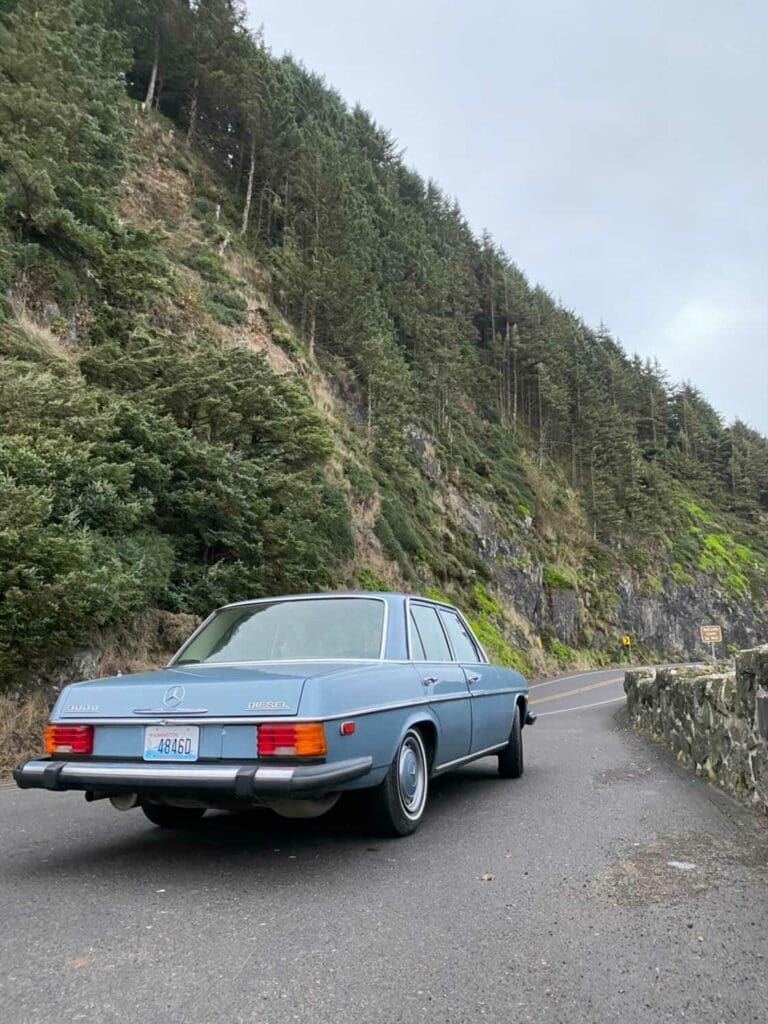Classic blue car parked near a rocky hillside under a cloudy sky.