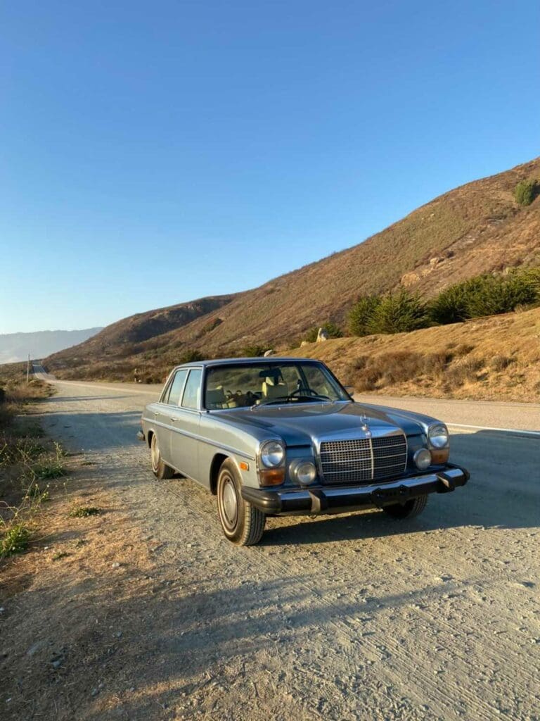 Classic silver convertible parked by a scenic desert road under clear blue sky.