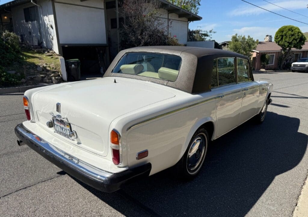 Classic white convertible car with a black soft top parked on a sunny street.