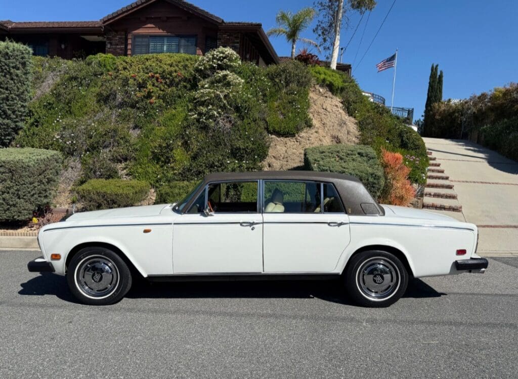 Classic white Rolls-Royce parked on a sunny street near a hillside house.