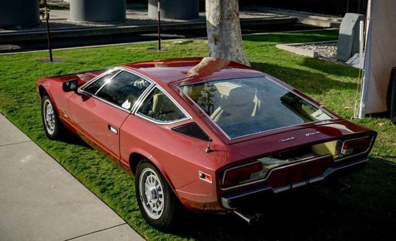 Classic red sports car parked under a tree on a sunny day.