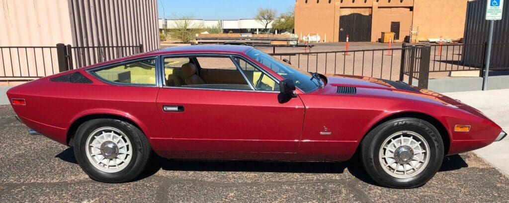 Classic maroon muscle car parked outdoors by a building.