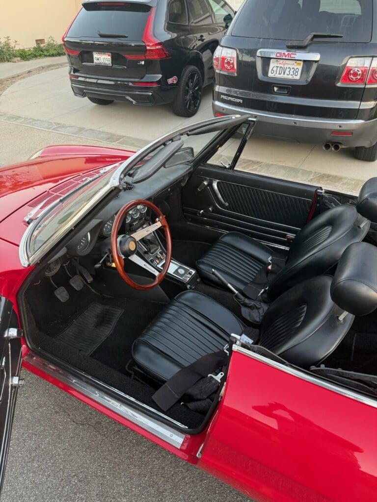 Red convertible sports car with black leather interior and wooden steering wheel.