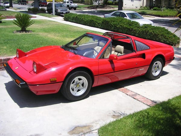 Red vintage sports car parked on a driveway in a sunny suburban area.