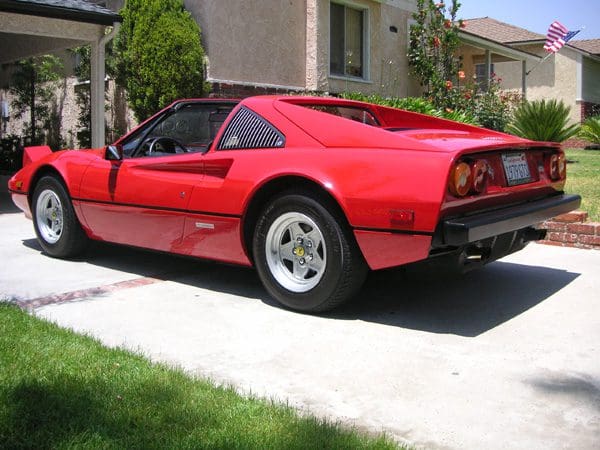 Classic red sports car parked on driveway near house.