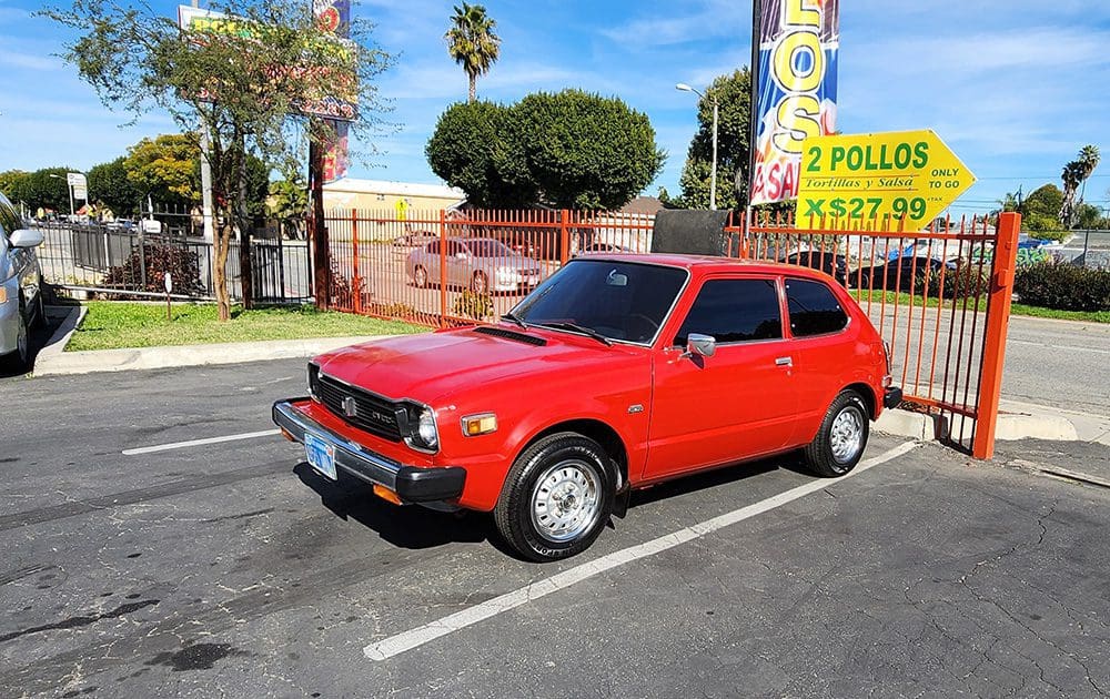 Classic red compact car parked in a sunny lot.