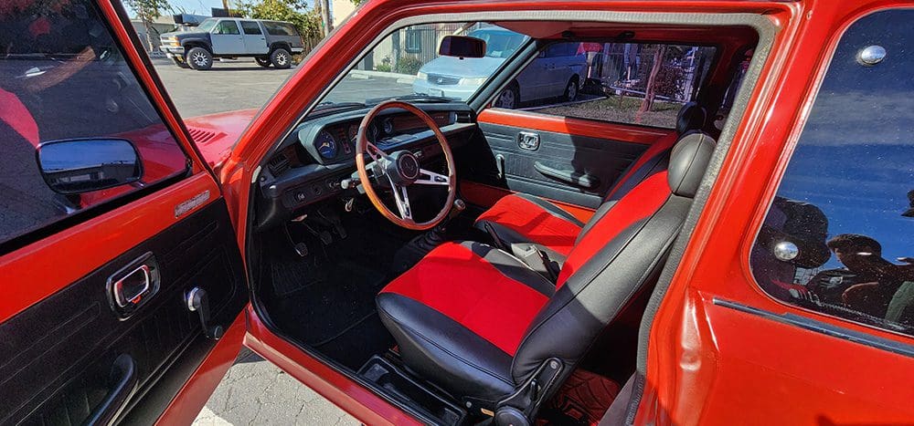 Classic car interior with red and black seats and wooden steering wheel.