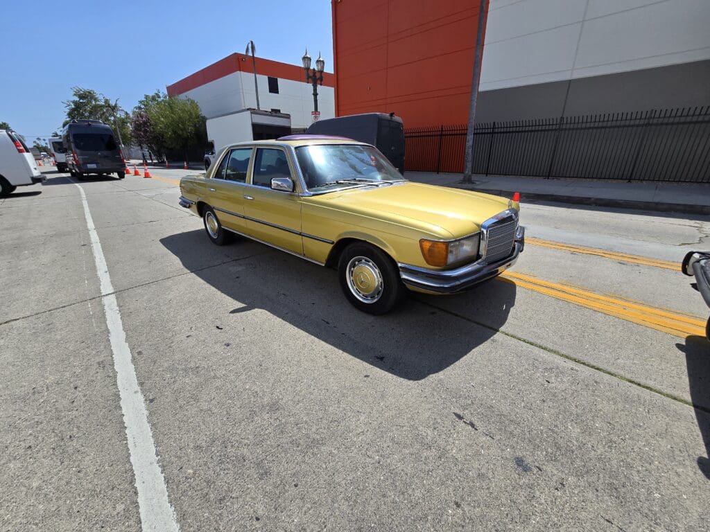 A vintage yellow car parked on a sunny street near a red and white building.
