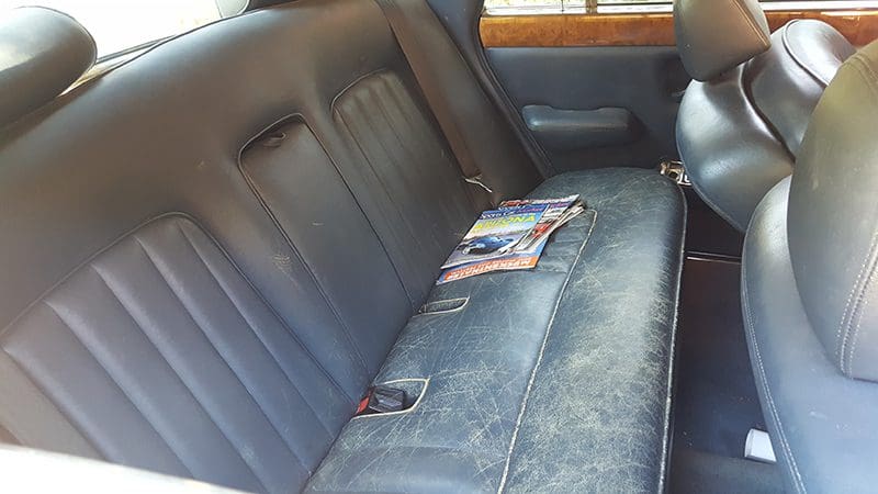 Worn leather car backseat with magazines scattered on it.