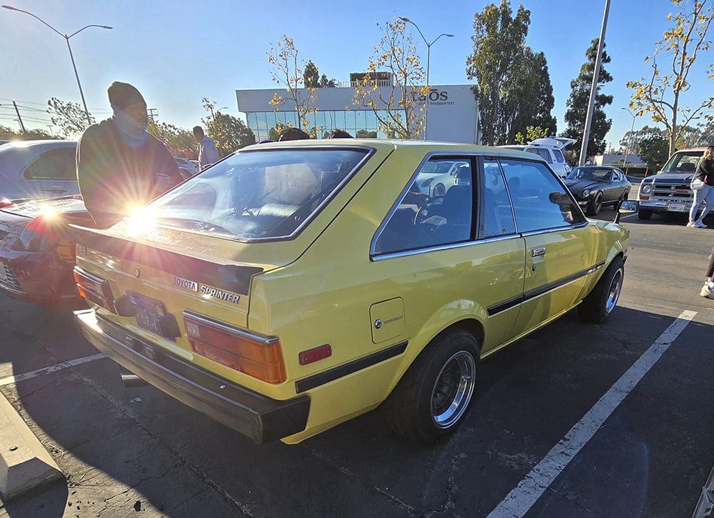 Yellow vintage hatchback car parked outdoors with sunlight glare.