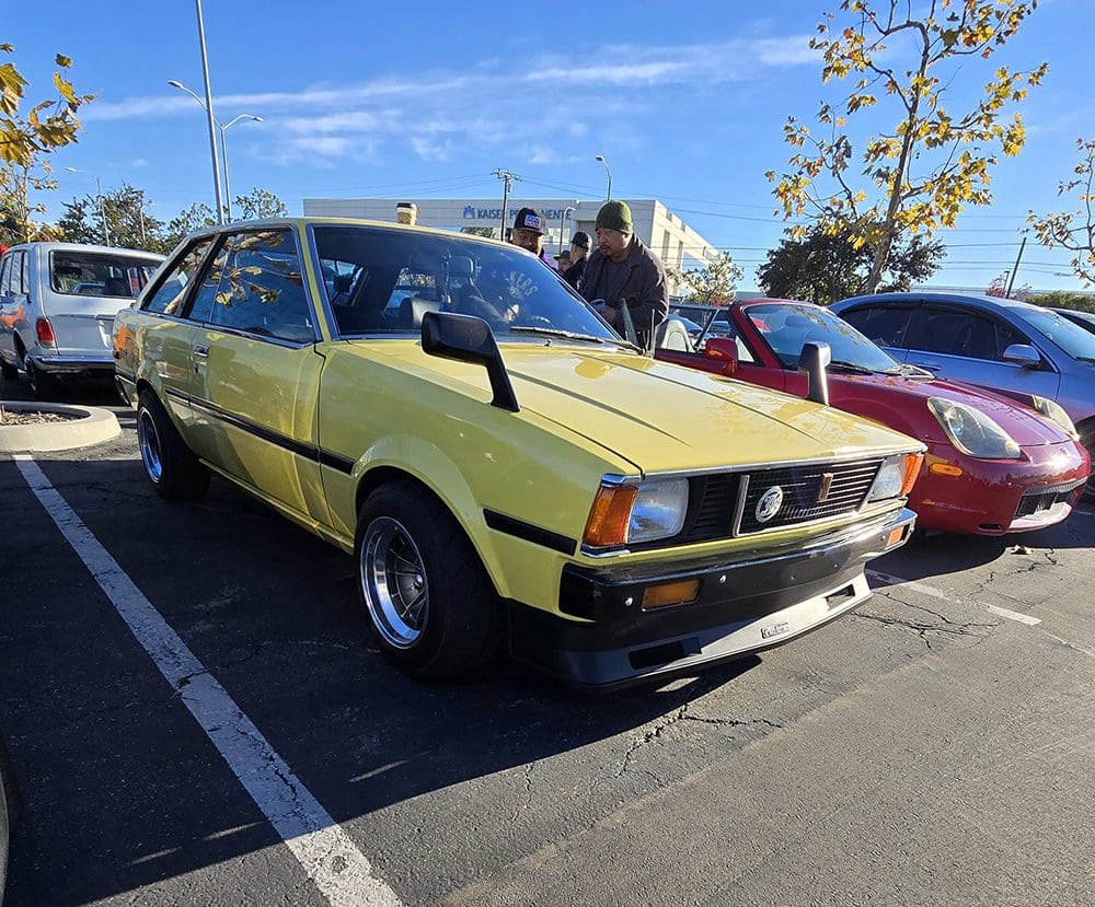 Yellow vintage car parked outdoors with people nearby.