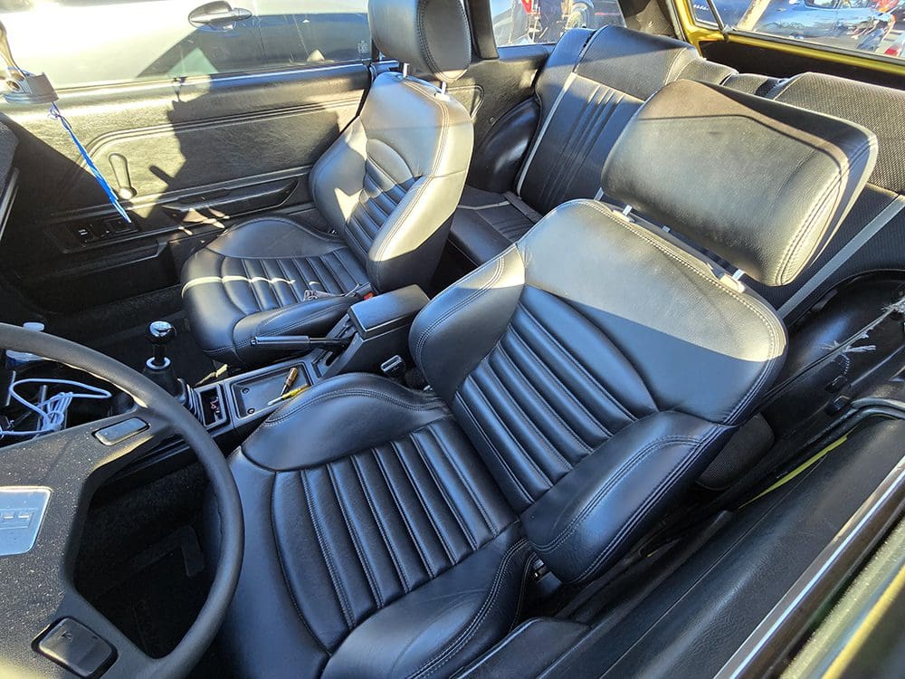 Interior of a classic car with black leather seats and detailed stitching.