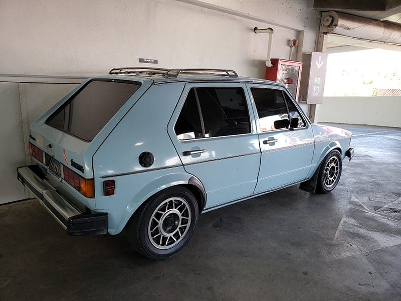 Light blue vintage hatchback parked indoors with sporty wheels.