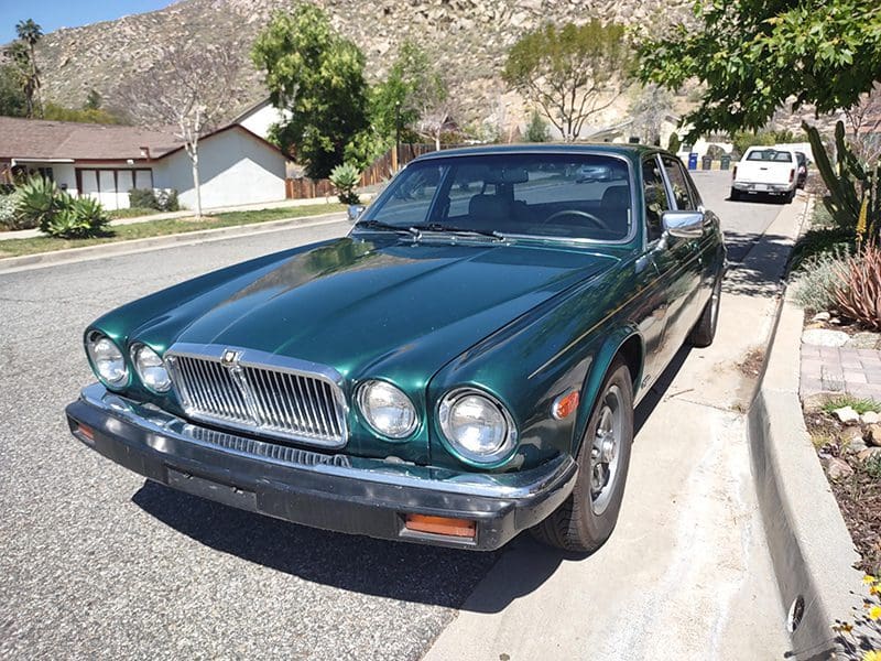 Classic green luxury car parked on a sunny suburban street.