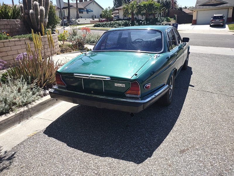 Classic green vintage car parked on a sunny suburban street.
