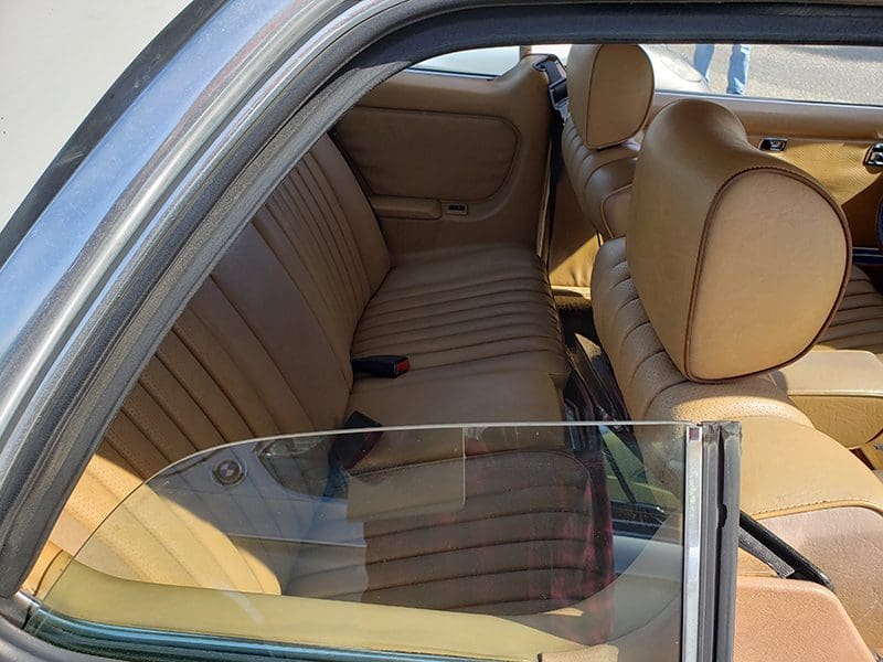 Interior rear seat of a classic car with tan upholstery.