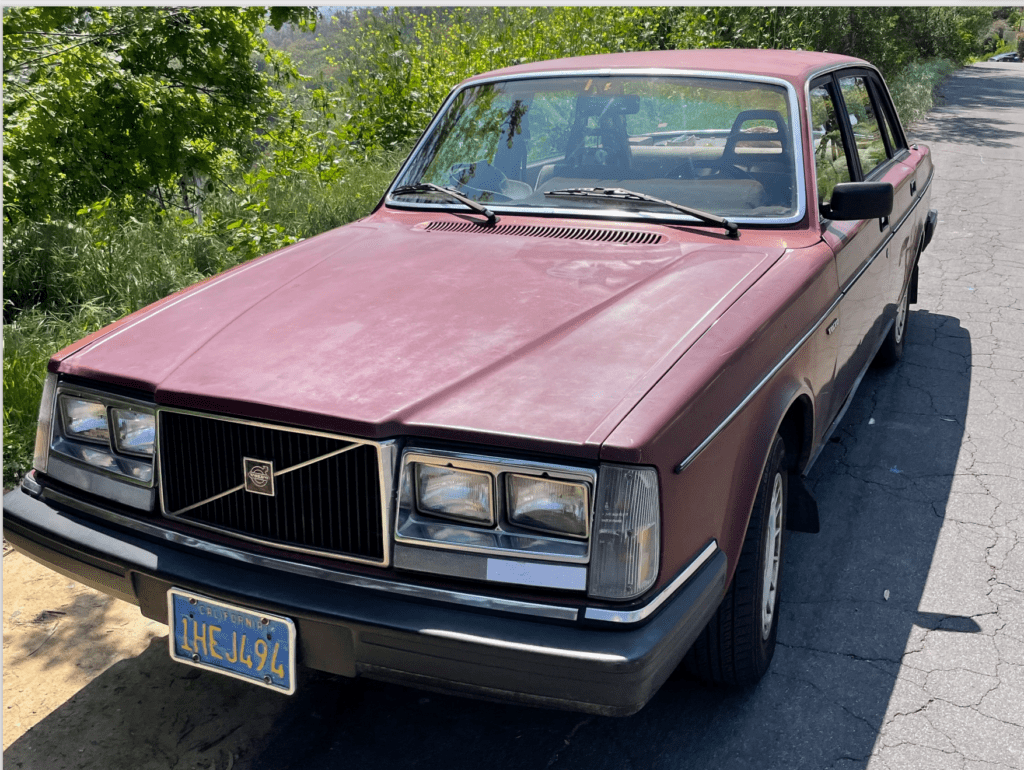 A dusty pink Volvo sedan parked on the street.