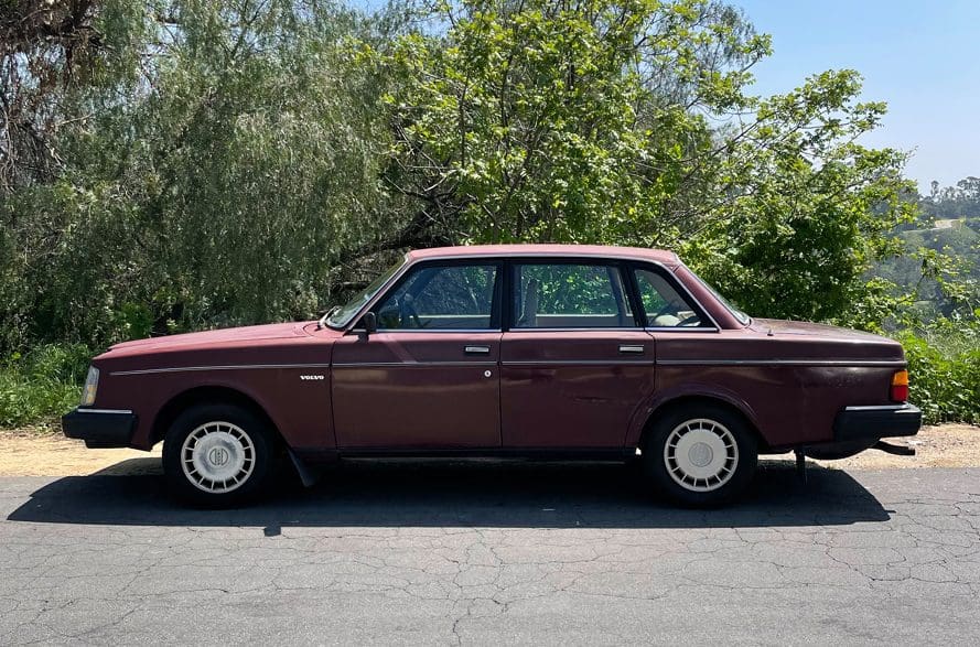 Classic maroon sedan parked beside green trees on a sunny day.