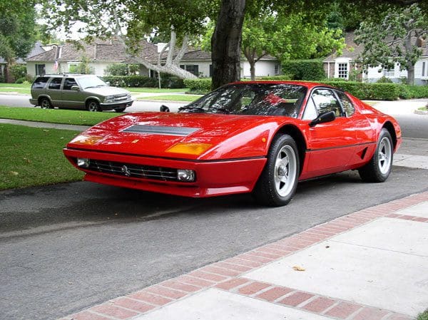 Red vintage sports car parked on a street near trees.