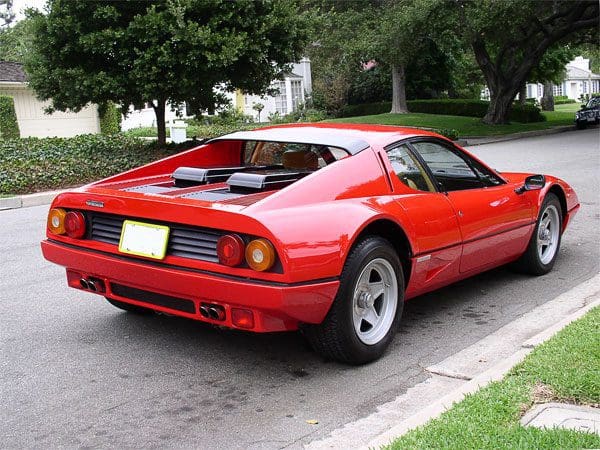 Red vintage sports car parked on a street near trees.