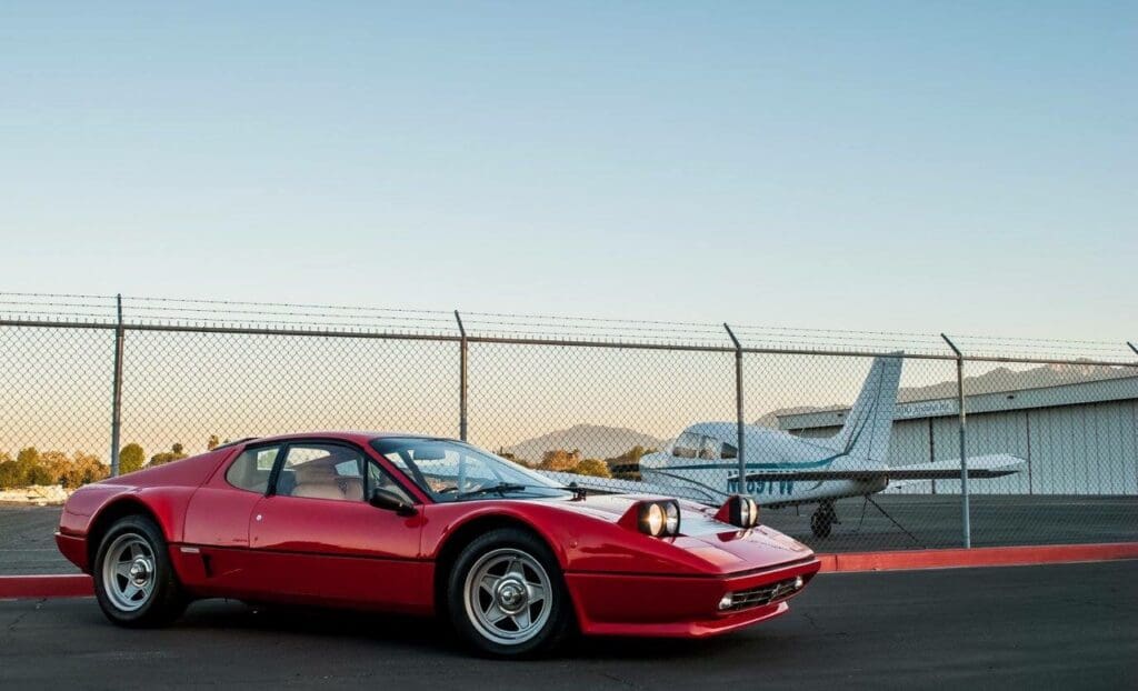 A red classic sports car parked near a small airplane at sunset.