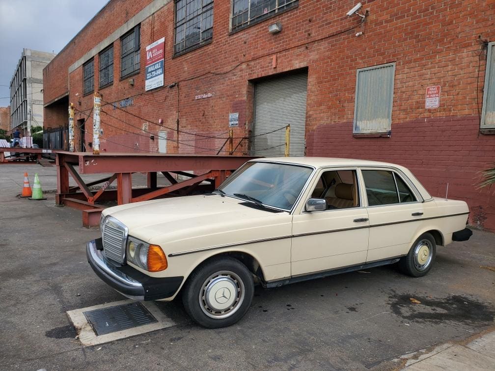 A vintage beige Mercedes-Benz parked by a brick building in an industrial area.