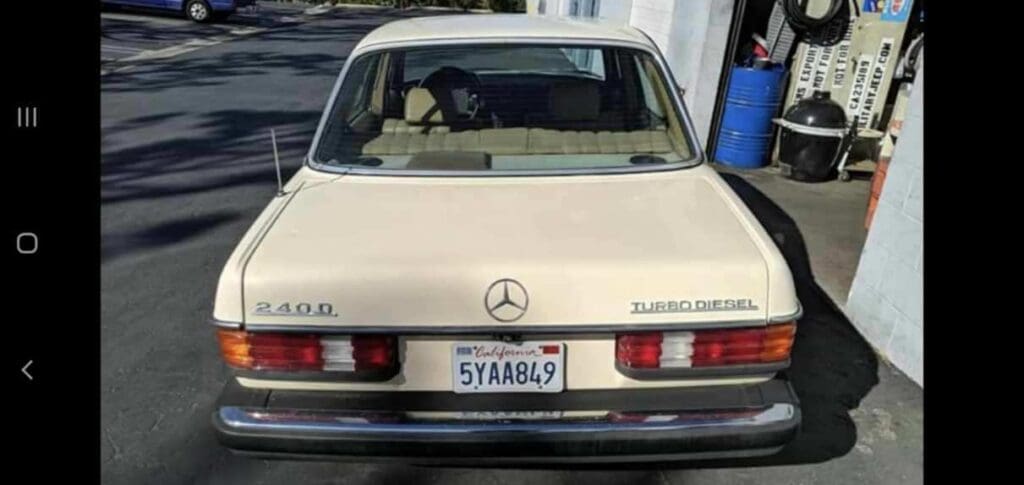 A vintage beige Mercedes-Benz parked by a brick building in an industrial area.