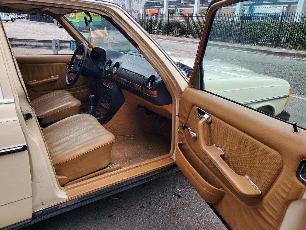 Interior view of a vintage tan car with open door showing seats and dashboard.