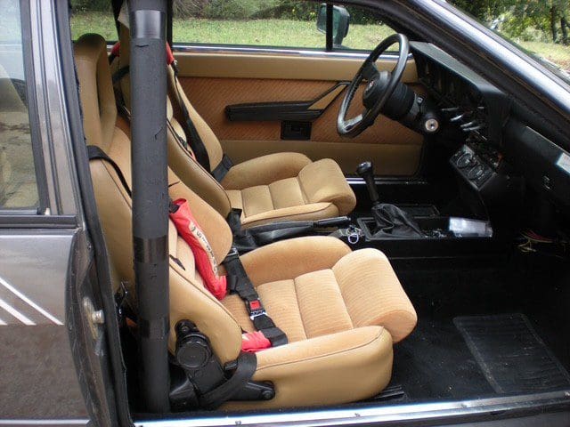 Two beige car seats with racing harnesses inside a vehicle.