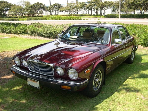 Classic maroon Jaguar parked on a sunny lawn.