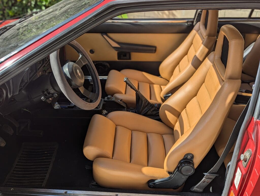 Interior of a vintage car with tan leather seats and a classic steering wheel.