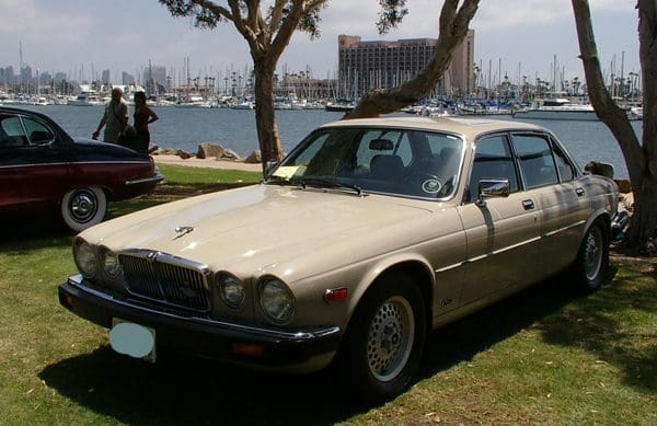 Classic beige Jaguar sedan parked on grass near waterfront with boats.