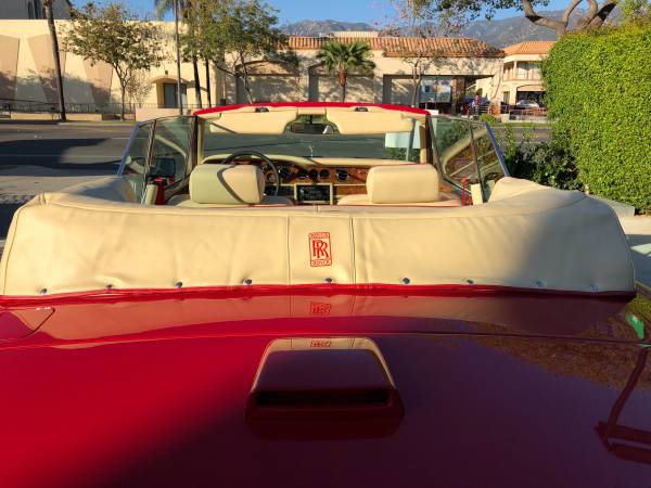 Rear view of a classic red convertible car with beige interior in a sunny neighborhood.