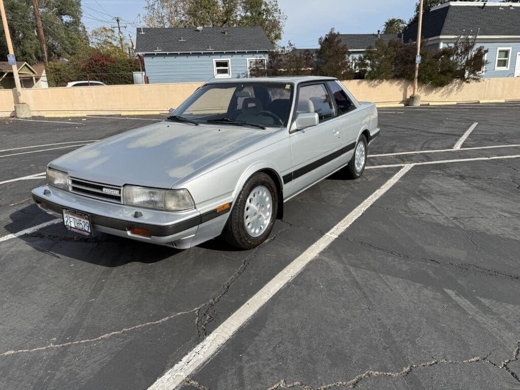 Silver classic coupe parked in an empty lot on a sunny day.