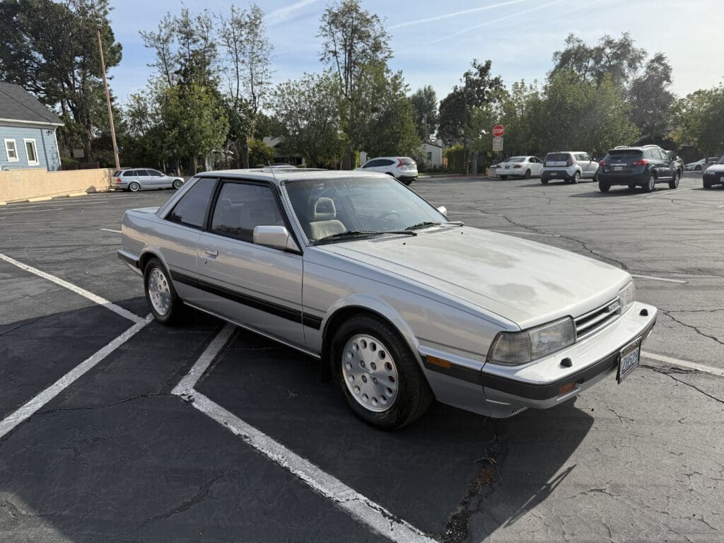 Classic silver coupe parked in an outdoor lot under daylight.