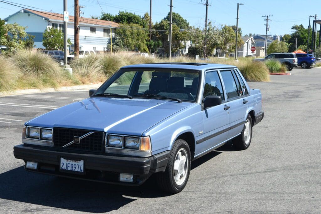 A classic blue Volvo sedan parked on a sunny suburban street.