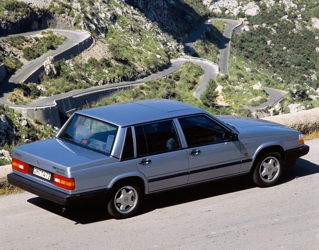 A classic silver sedan parked on a winding mountain road.