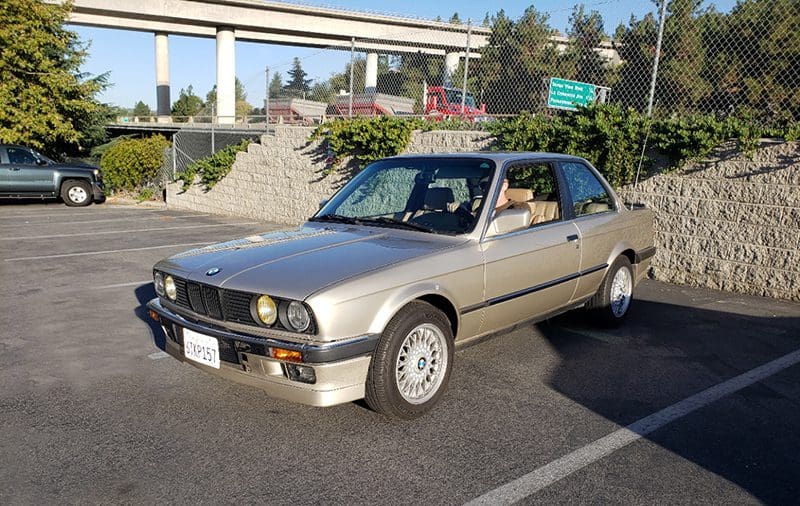 Classic silver BMW sedan parked outdoors near a bridge.